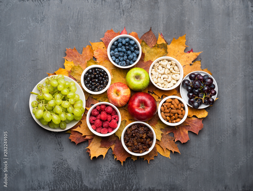 Seasonal autumn background. Frame of colorful maple leaves, raisins, nuts and berries over grey