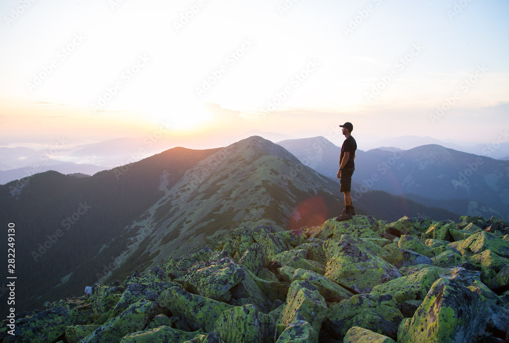 caucasian man hiker is on the peak of green stones mountain enjoy a panoramic view of mountains in the sunset light