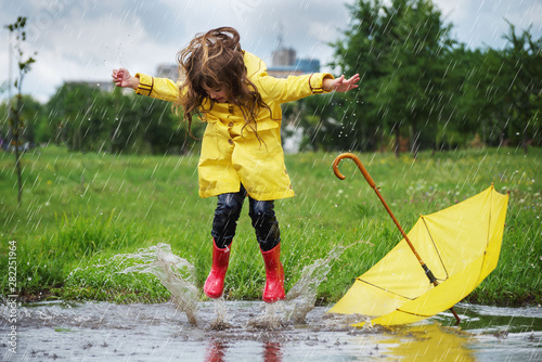 Tela Happy child girl with an umbrella and rubber boots in puddle  jump