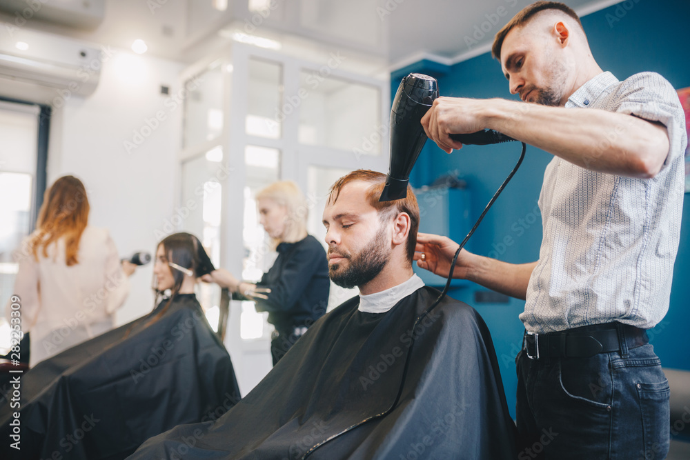 young bearded man getting groomed hairdresser with hair dryer barbershop. Professional Hairdresser Drying Hair Handsome Client. Professional Barber Working In Hairdressing Salon, Use Hair Dryer
