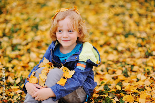 baby - little boy with curly blond hair smiling against the background of yellow autumn leaves in the Park