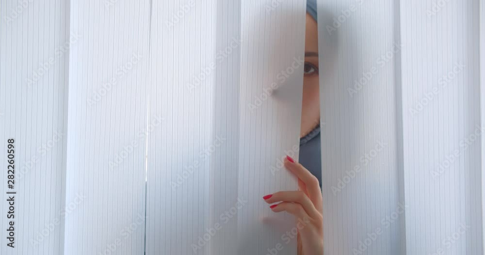 Closeup portrait of young muslim woman in hijab looking looking at camera hiding behind tulle indoors in apartment Closeup portrait of young muslim woman in hijab looking looking at camera hiding behind tulle indoors in apartment