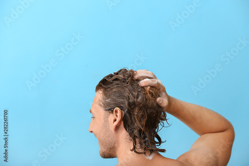 Handsome young man washing hair against color background