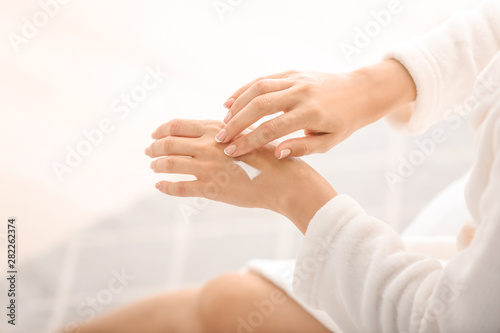 Young woman applying natural cream onto skin at home