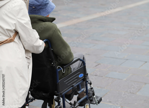 Closeup of elderly disabled woman  in wheelchair assists by female assistant.
