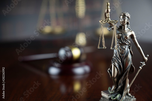 Justice concept. Themis statue, judge's gavel and scale of justice on the gray background.