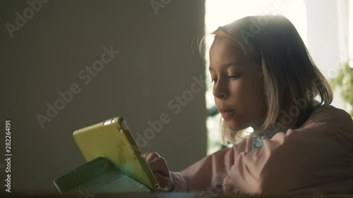 Cute kid girl using tablet computer, young teenage child doing homework on digital tablet drink milkshake in restaurant after lessons photo