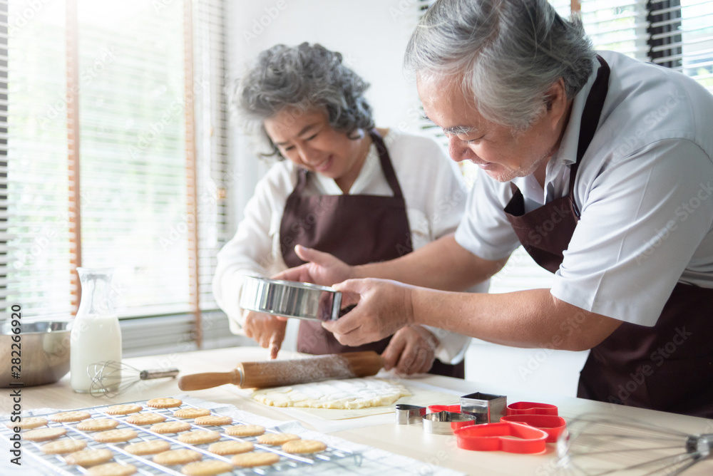 Happy Asian senior couple in brown aprons baking cookies together. Happy Asian senior couple in brown aprons baking cookies together.
