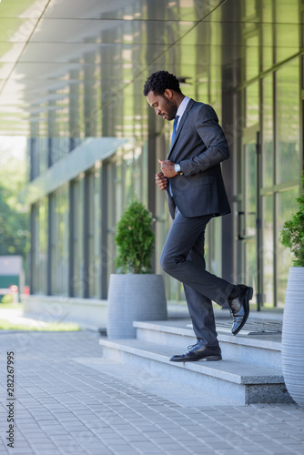 handsome african american businessman in suit walking on stairs of office building