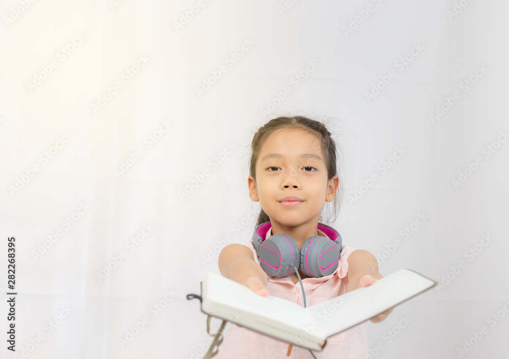 Happy little girl kid standing with headphones and hand holding book Happy little girl kid standing with headphones and hand holding book
