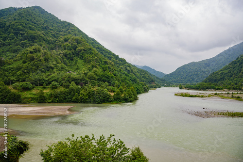 River flowing in the mountains, a mountain river, green trees on the mountains on a cloudy day, with clouds in the sky.