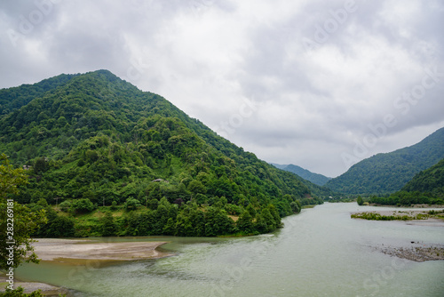 River flowing in the mountains, a mountain river, green trees on the mountains on a cloudy day, with clouds in the sky. photo