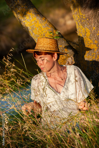 WELLNESS, RELAXATION, WOMAN WITH A STRAW HAT IN THE GRASS IN THE COUNTRYSIDE.