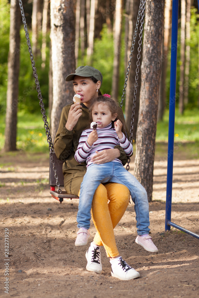 Mother and daughter sitting on teeter-totter, in the park, eating ice cream. Mother and daughter sitting on teeter-totter, in the park, eating ice cream.