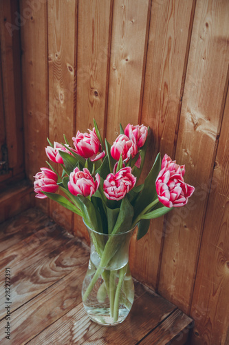 Bouquet of flowers in a vase on a wooden table by the window. Tulips in a vase by the window.