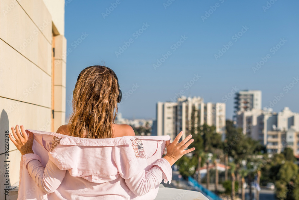 woman in a pink shirt on the balcony dancing and listening music in a headphones against the city background woman in a pink shirt on the balcony dancing and listening music in a headphones against the city background