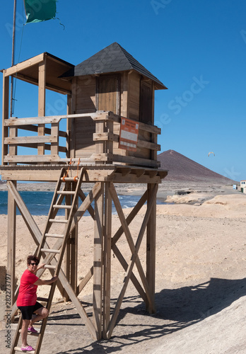an elderly lady climbs the ladder to reach the lifeguard's post. Beautiful landscape with blue sky and sea. wind and waves for surf and kitesurf enthusiasts.