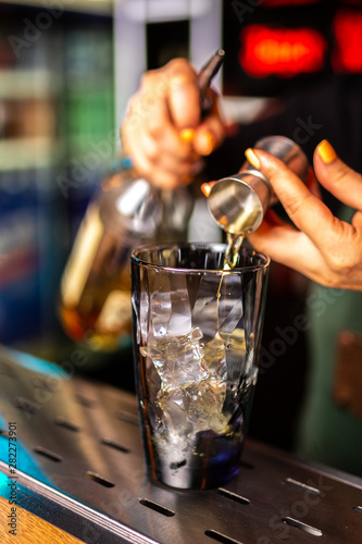 Close-up of expert bartender making cocktail in bar, splash of whiskey and rum.