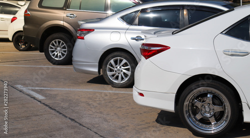 Closeup of rear, back side of white car with other cars parking in outdoor parking lot in sunny day. 