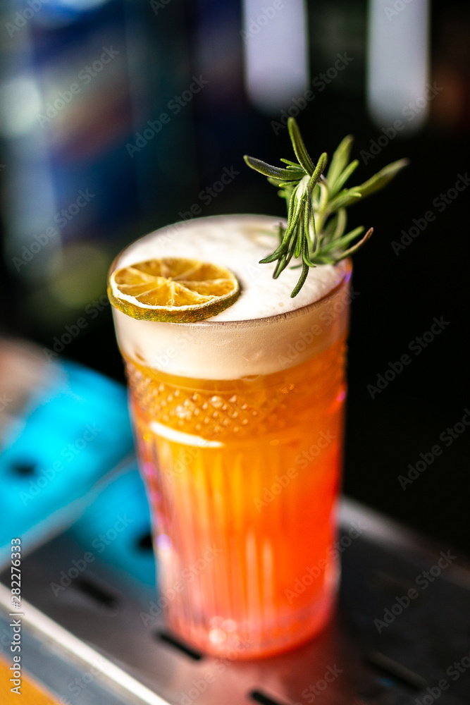Close-up orange cocktail with dried lemon and rosemary on the bar, blurred background. Close-up orange cocktail with dried lemon and rosemary on the bar, blurred background.