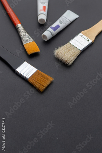 brushes and paint tubes closeup on black table with soft-focus and over light in the background