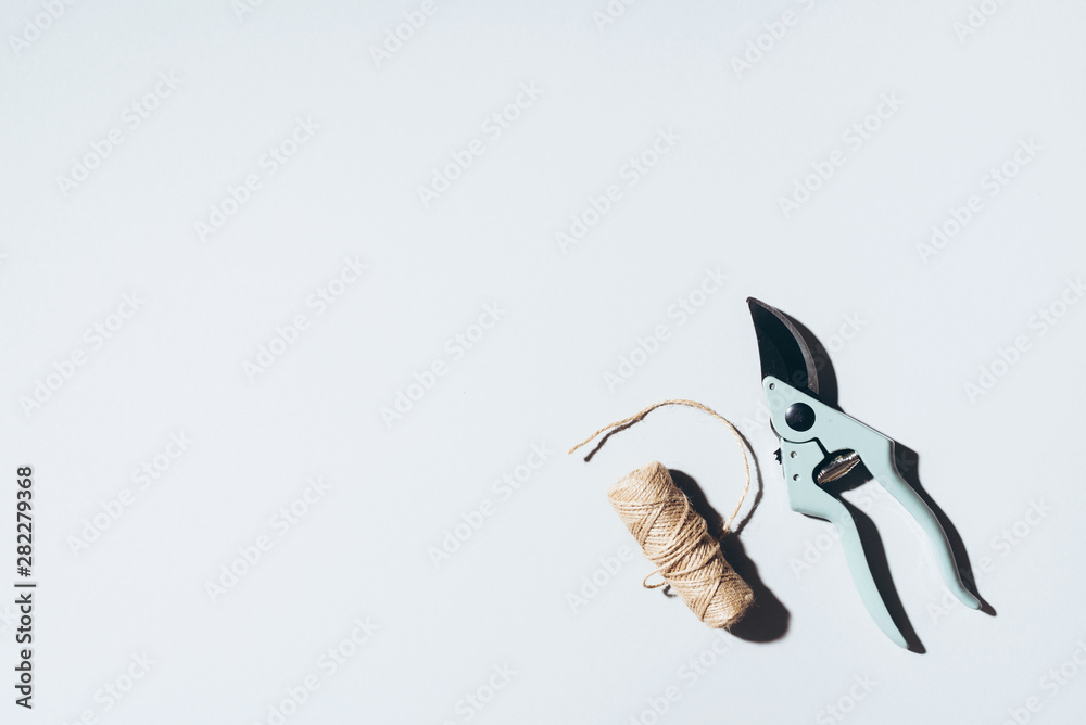 Obraz premium Branch pruner and craft linen threads over grey background. Gardening tools. Spring still life.