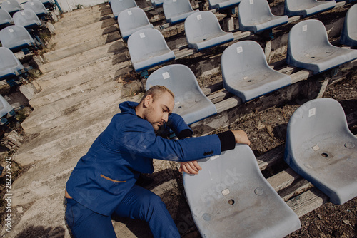 Man in blue suit sleeping after hard work cycle on fan tribune on stadium © vitleo