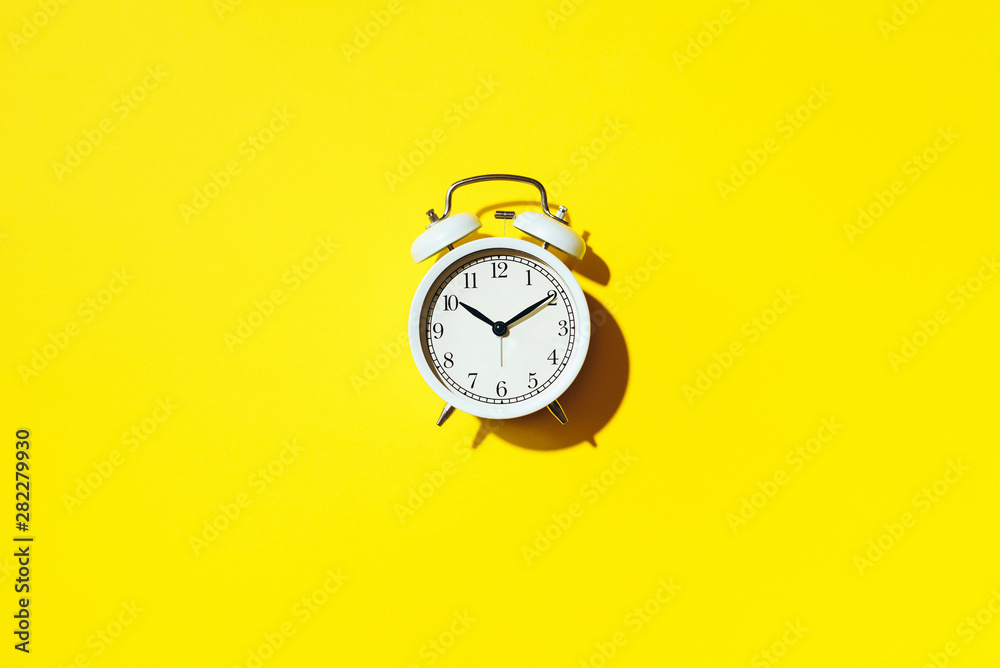 White alarm clock with hard shadow on yellow background. Top view. Wake up alert concept. Morning routine. White alarm clock with hard shadow on yellow background. Top view. Wake up alert concept. Morning routine.