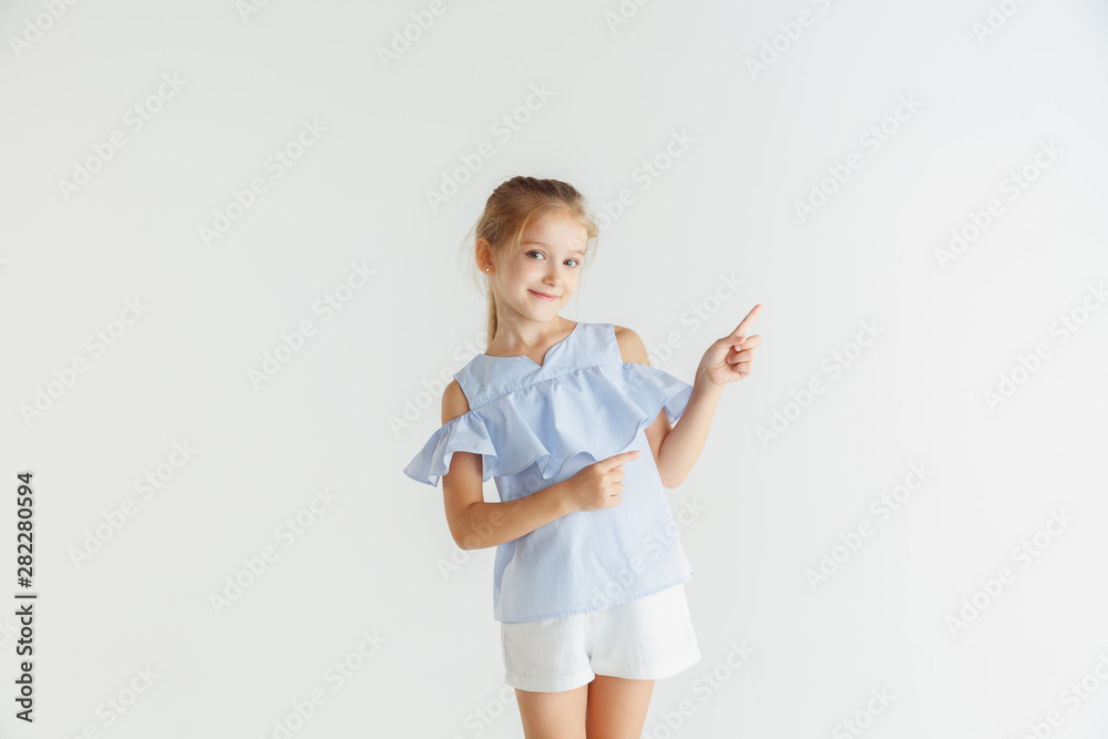Stylish little smiling girl posing in casual clothes isolated on white studio background. Caucasian blonde female model. Human emotions, facial expression, childhood. Pointing on empty space bar. Stylish little smiling girl posing in casual clothes isolated on white studio background. Caucasian blonde female model. Human emotions, facial expression, childhood. Pointing on empty space bar.