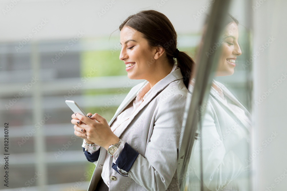 Pretty young business woman stands on the stairs at the office and use mobile phone Pretty young business woman stands on the stairs at the office and use mobile phone