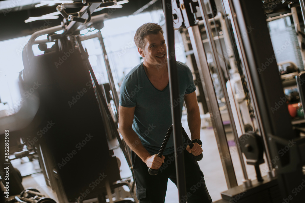Young sporty man working out on pull-down machine in gym Young sporty man working out on pull-down machine in gym