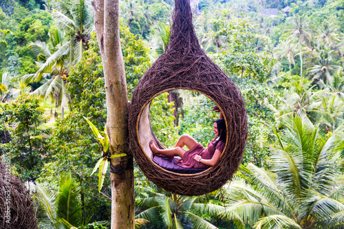 A female tourist is sitting on a large bird nest on a tree at Bali island photo