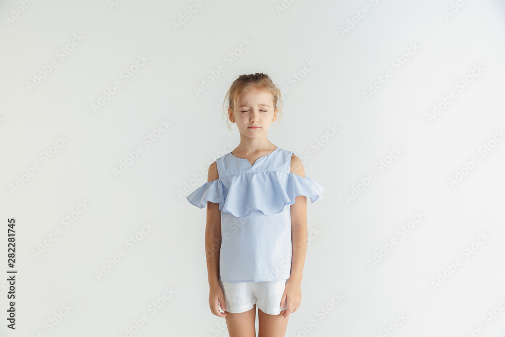 Stylish little smiling girl posing in casual clothes isolated on white studio background. Caucasian blonde female model. Human emotions, facial expression, childhood. Standing with eyes closed. Stylish little smiling girl posing in casual clothes isolated on white studio background. Caucasian blonde female model. Human emotions, facial expression, childhood. Standing with eyes closed.