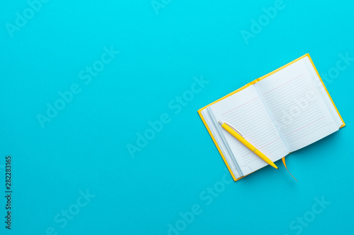 Fotografie Top view photo of opened notebook and yellow pen over it on turquoise blue background with copy space