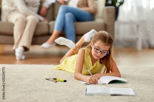 education, school and learning concept - student girl lying on floor and writing to notebook at home