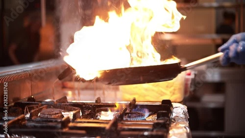 Chef is holding pan or wok and stirring or cooking with fire or flames