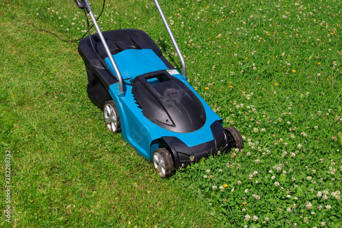 Electric lawn mower on a grass lawn with half mowed grass