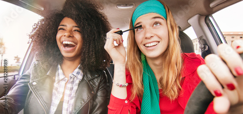 fun in car girl friends driving having fun and laughing. concept of reckless driving woman doing make up while driving with afro hair girl on passenger seat