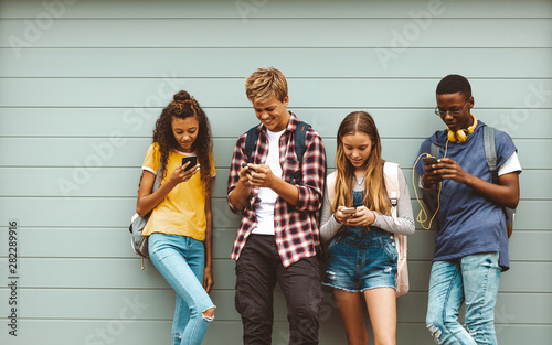 Teenage boys and girls using cell phones standing outdoors photo