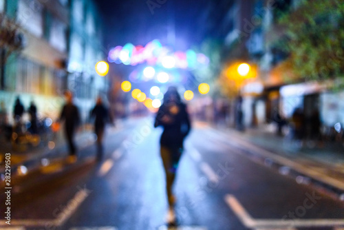 Urban night scene with people walking out of focus with colored background.
