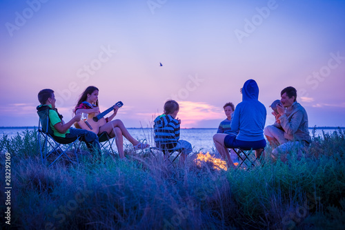 people sitting on the beach with campfire at sunset