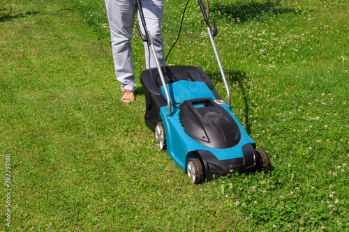 Woman gardener with an electric lawn mower on a grass lawn with half mowed grass with copyspace