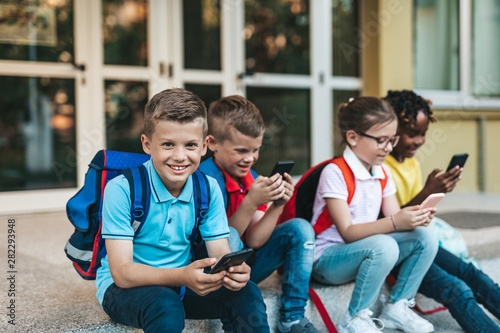 Group of happy elementary school students with smartphones. Primary education, friendship, childhood, and technology concept. photo