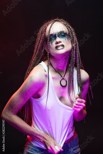 Emotional photo of a beautiful young slim girl with creative make-up and a hairstyle of cornrows, wearing white t-shirt on a black. Conceptual, commercial, advertising design