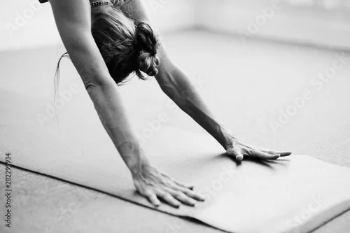 Fototapeta na wymiar Classical black and white Art Photography of a woman practicing advanced yoga pose indoors on a yoga mat.  Woman's dynamic arms in Downward Dog.