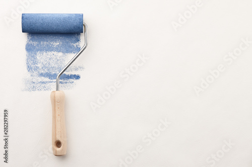 Roller with blue paint on wallpaper background