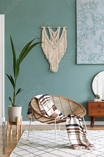 Stylish and boho composition of living room with design armchair, wooden retro commode with mirror, cement pot with plant, beige macrame, plaid and elegant accessories. Modern home decor. Template.