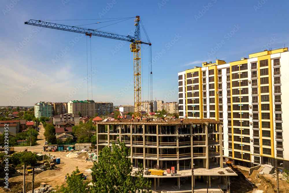 Apartment or office tall building under construction. Working builders and tower cranes on bright blue sky copy space background.