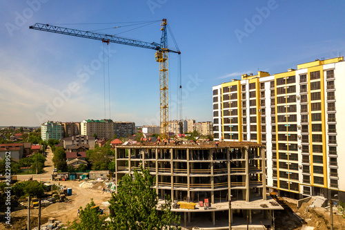 Apartment or office tall building under construction. Working builders and tower cranes on bright blue sky copy space background. © bilanol