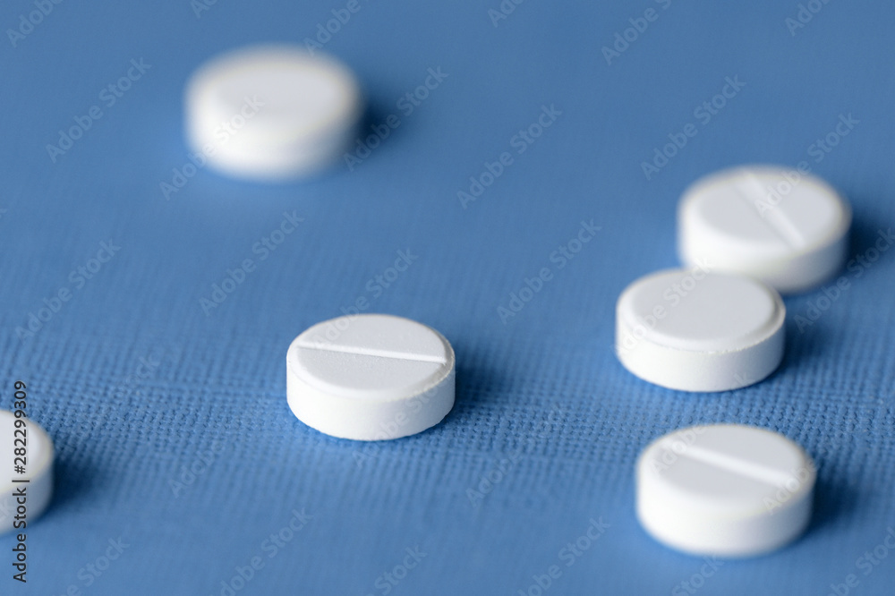 White tablets scattered on a blue background close up White tablets scattered on a blue background close up